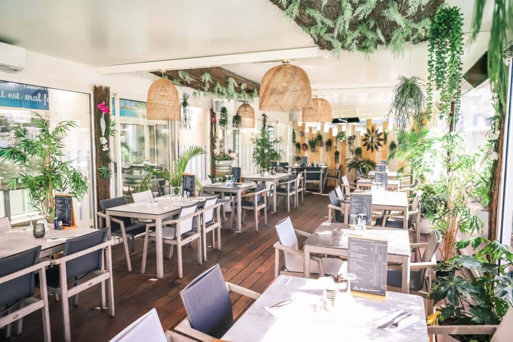 Bien éclairé, parquet, tables blanches, plantes vertes. Accueil chaleureux pour tous les invités.