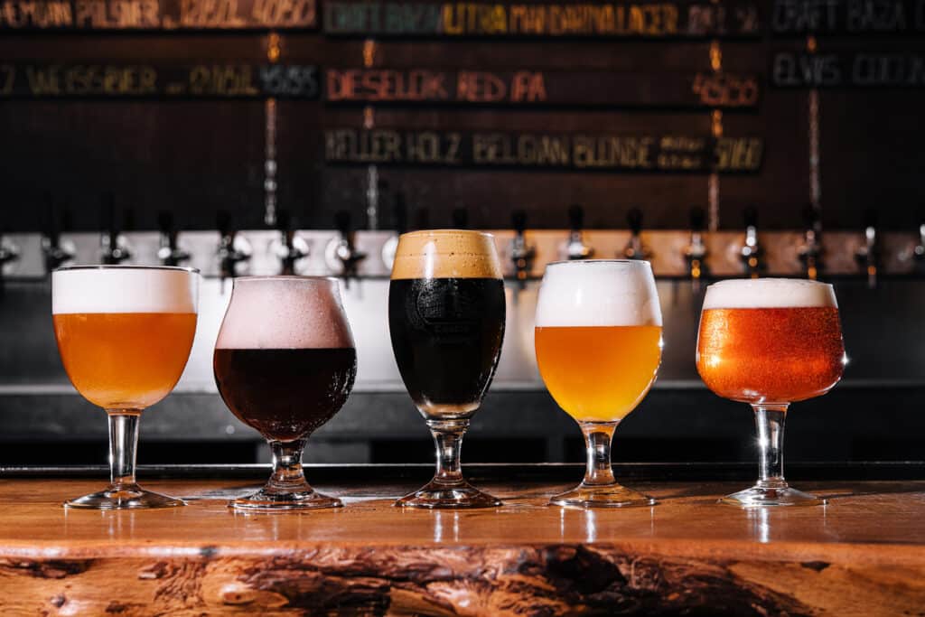 Cinq verres de bière alignés sur un comptoir captent l’ambiance animée d’un bar de Fréjus.