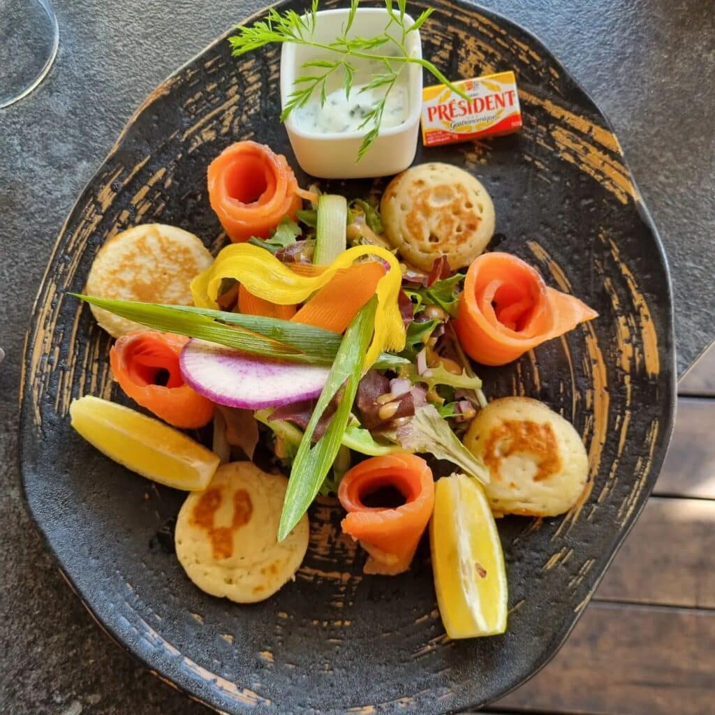 Assiette chez L'Évasion : saumon fumé, citrons, crêpes, verdure, radis, sauce et beurre.