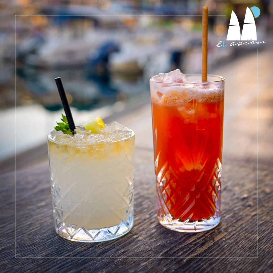 Deux cocktails sur table en bois, marina floue. Fréjus, lieu idéal pour se détendre à L'Évasion.