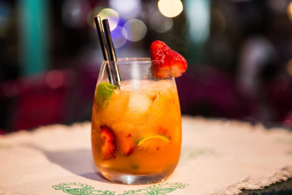 Un cocktail avec glace, fraises, citron vert, pailles noires ; des lumières colorées floues évoquent le bar L'Évasion.