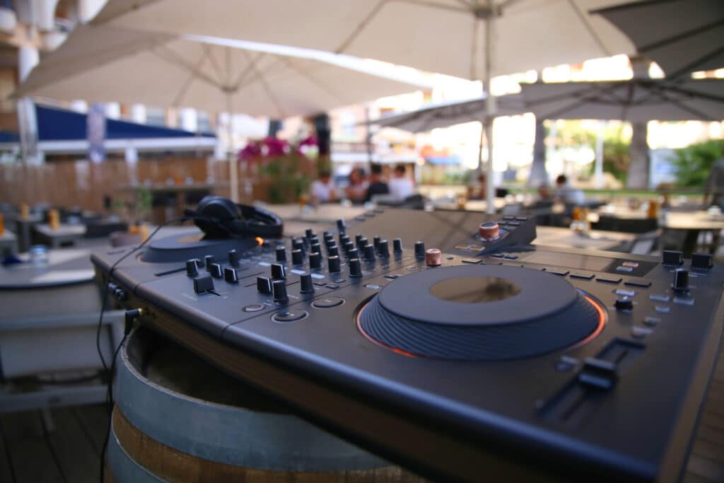 Contrôleur DJ sur un tonneau au bar extérieur à Fréjus, tables et parasols avec des gens flous.