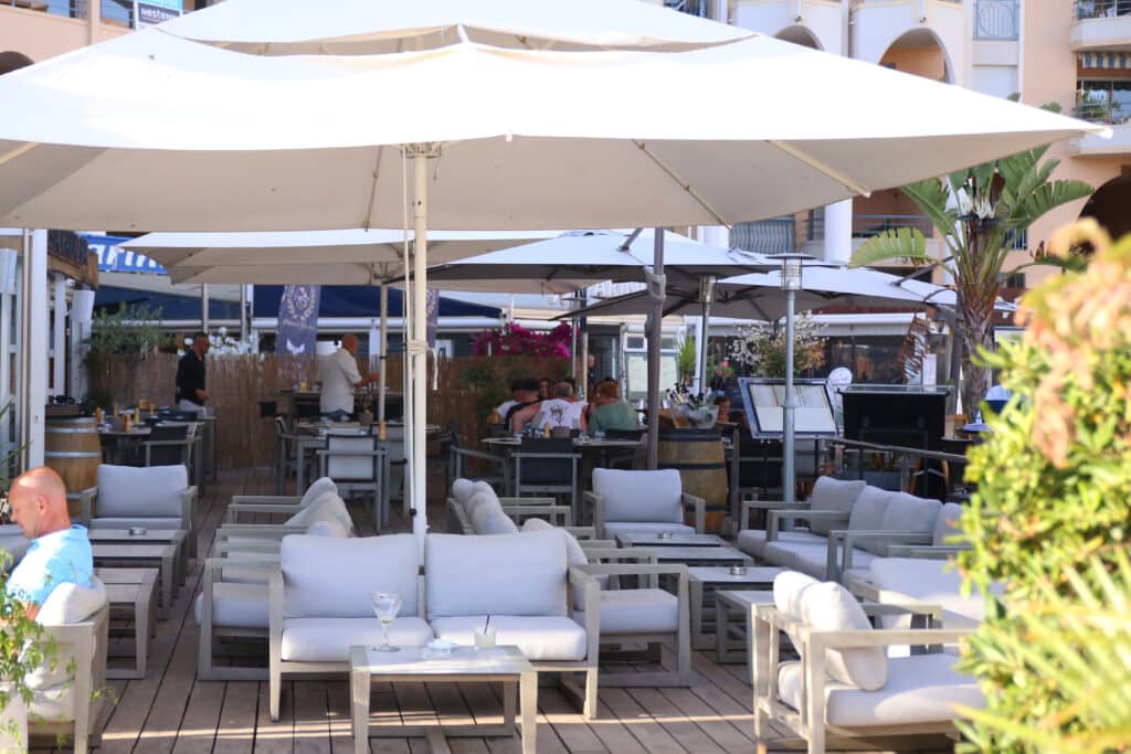 Terrasse avec sièges blancs, grands parasols, bar lounge. Découvrez le charme de Fréjus.