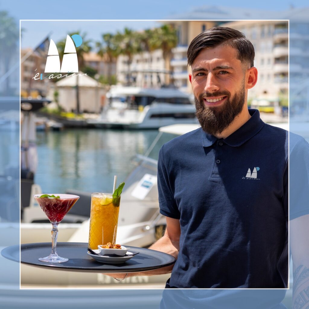 Homme polo bleu marine, plateau cocktails, marina de Fréjus, restaurant L'Évasion. Bateaux en arrière-plan.