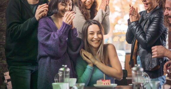 Groupe autour d'une femme souriante devant un gâteau d'anniversaire sur la terrasse de L'Évasion, Fréjus.